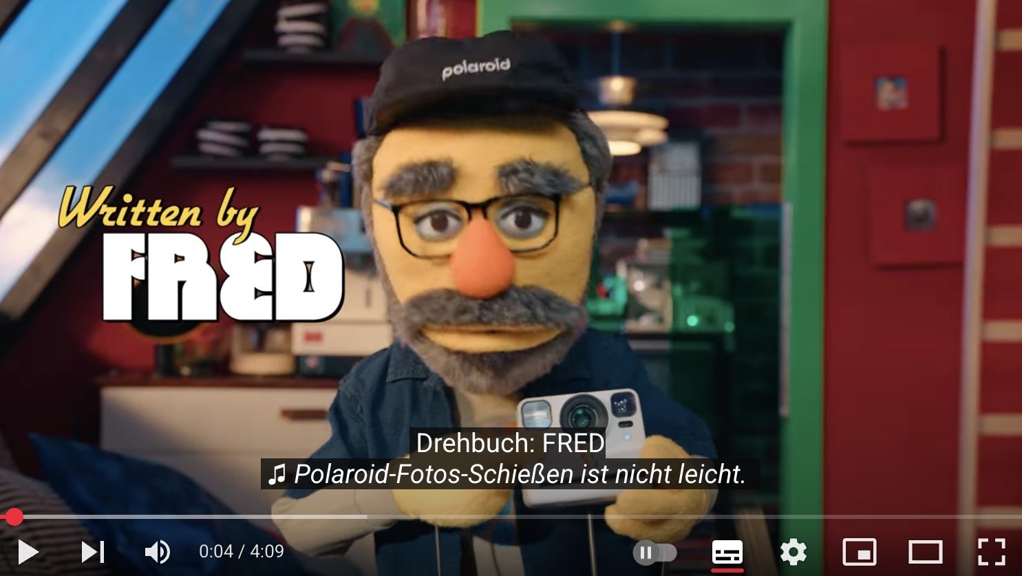 Still of Polaroid Youtube film with Fred the puppet holding a Polaroid camera.